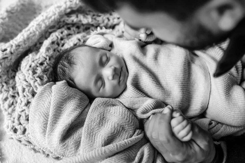 A sleeping newborn baby wrapped in cozy knit blankets rests peacefully in black and white photography.