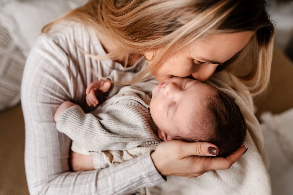 Tender moment between caregiver and sleeping baby in soft grey sweater.