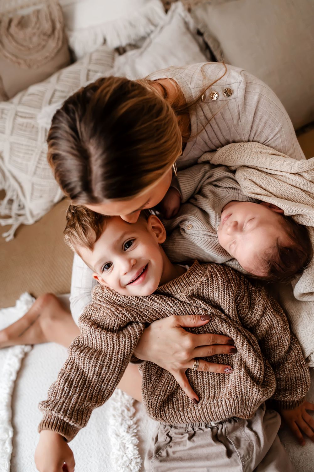 A sweet family moment featuring a mother and children cuddling together on a cozy bed with soft textiles.