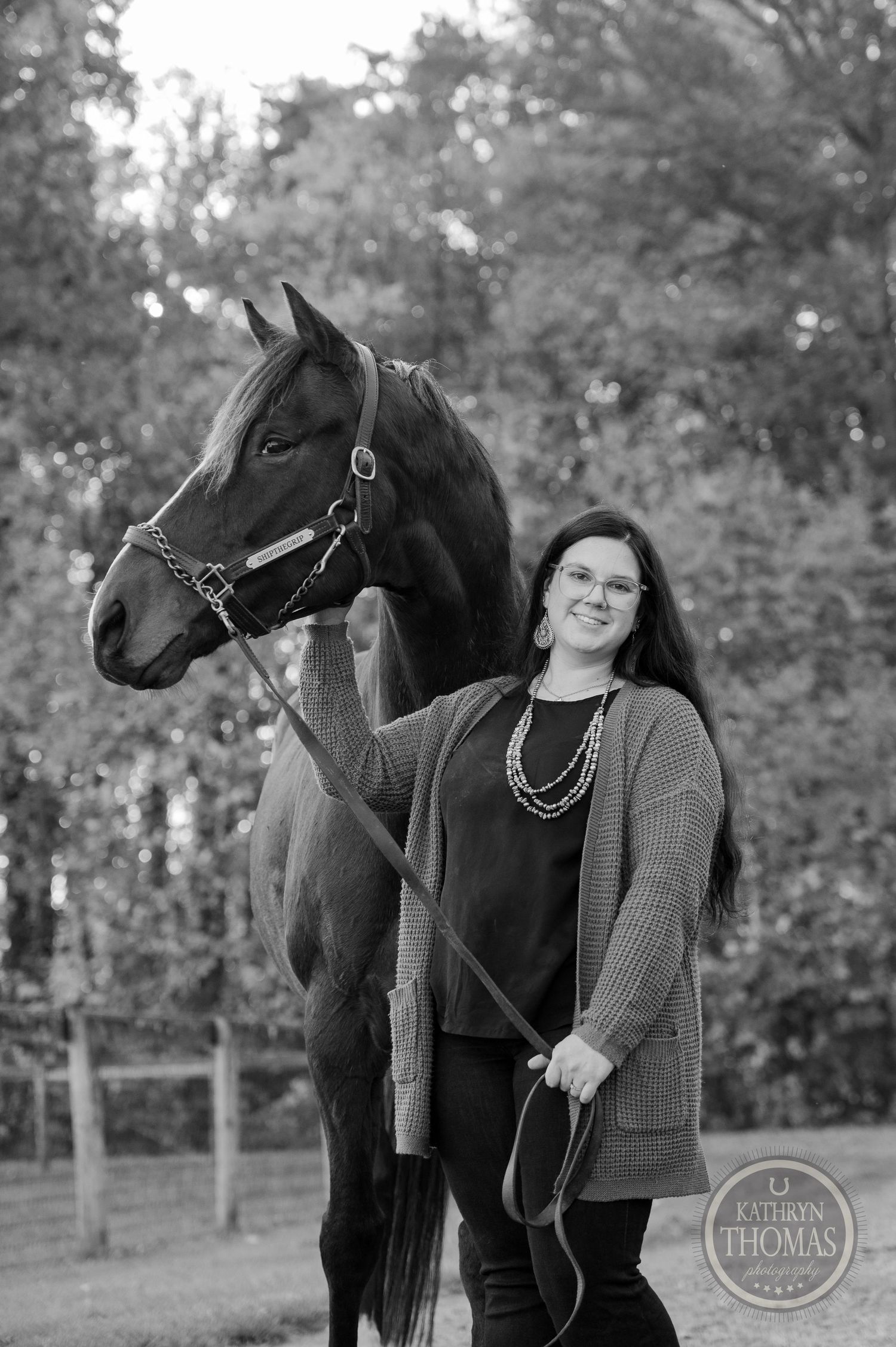 A black and white portrait of a person standing beside their horse in casual attire.