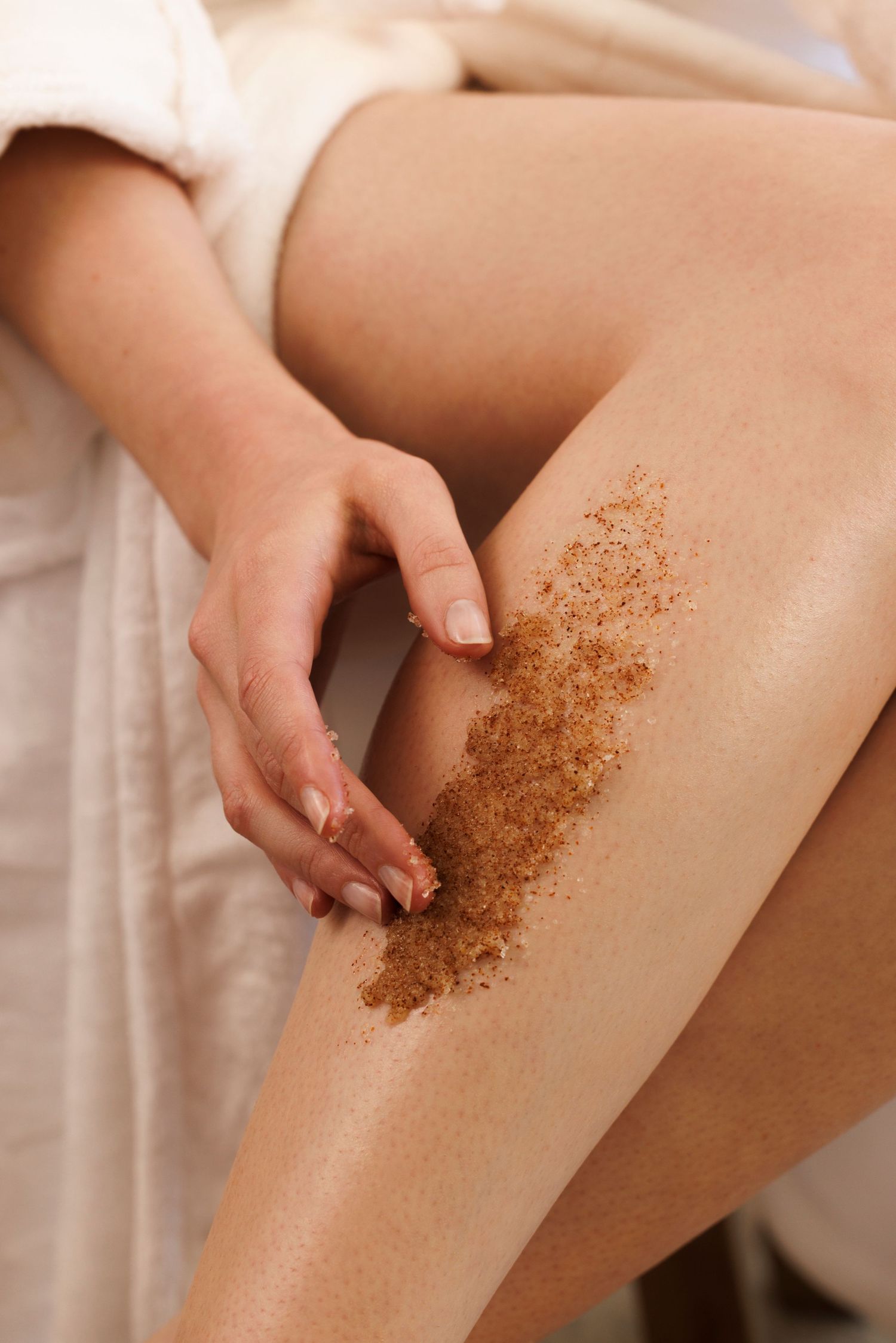 Person applying coffee scrub exfoliant to leg during skincare routine.