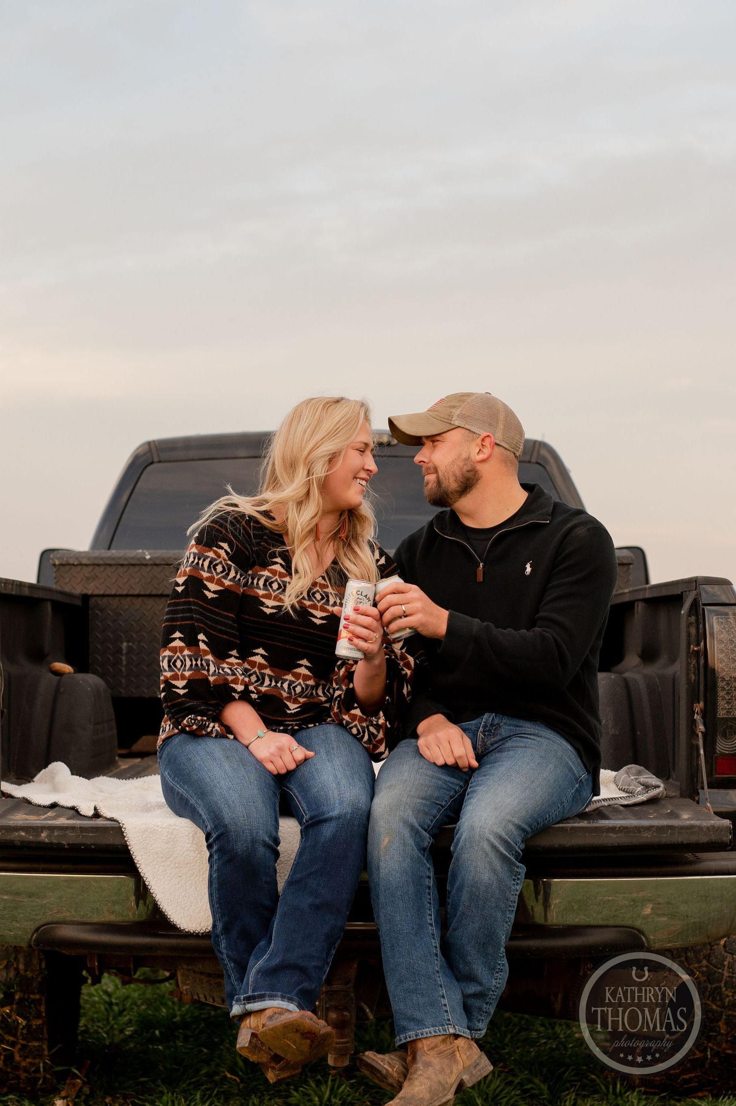 A couple shares a laugh while sitting together on a pickup truck tailgate at sunset.