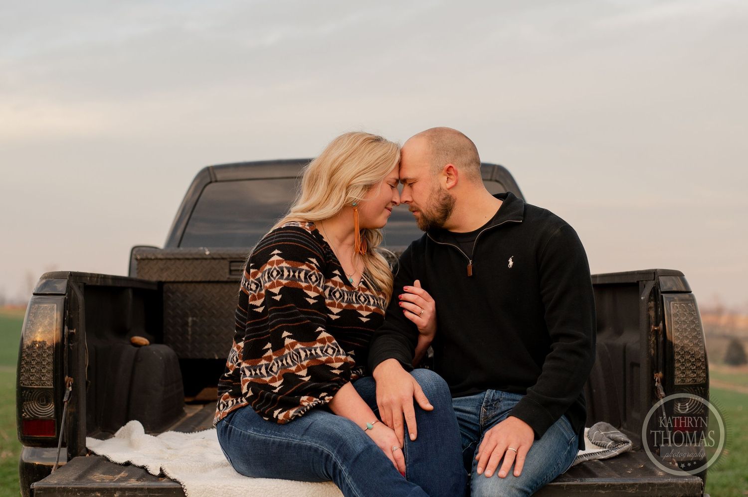 A couple shares an intimate moment while sitting in the back of a pickup truck at dusk.