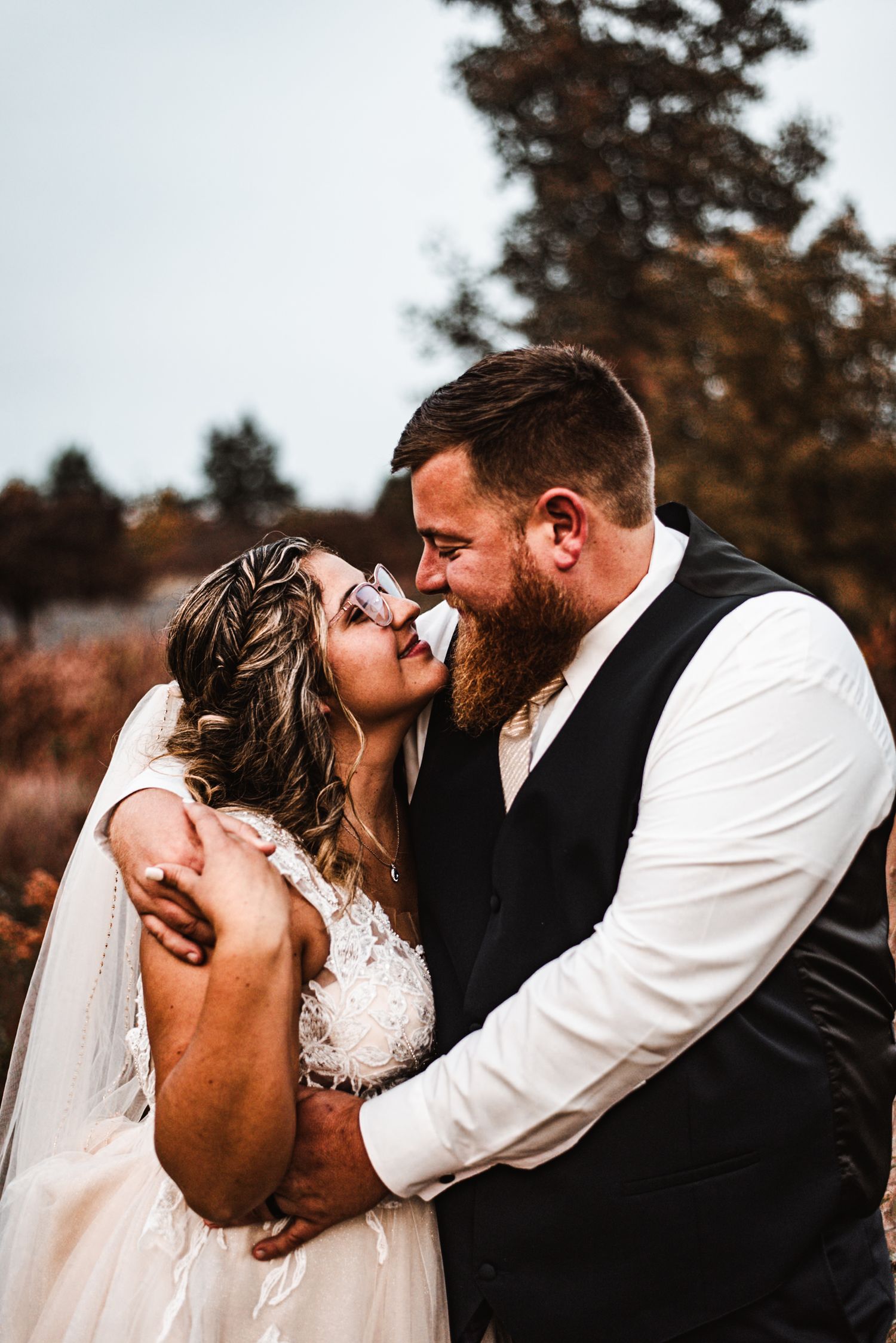 Romantic autumn wedding photo shows a loving couple sharing an intimate moment outdoors with fall foliage in background.