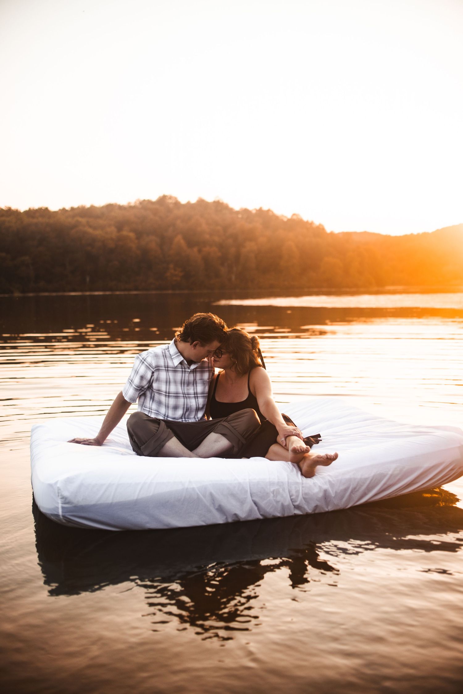 Couple relaxing on floating mattress in lake during golden hour sunset.