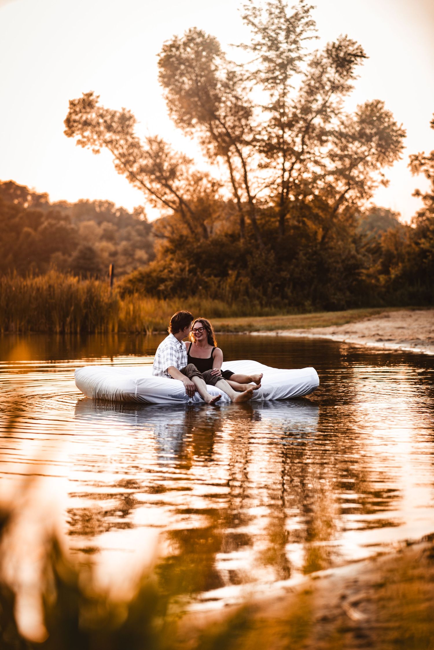 Romantic couple lounging on floating mattress in tranquil lake waters at sunset.