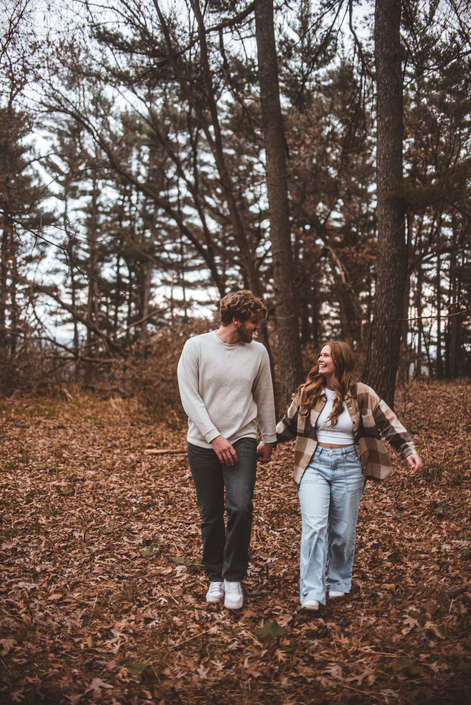 A couple walking together through fallen autumn leaves in a pine forest on a cozy fall day.