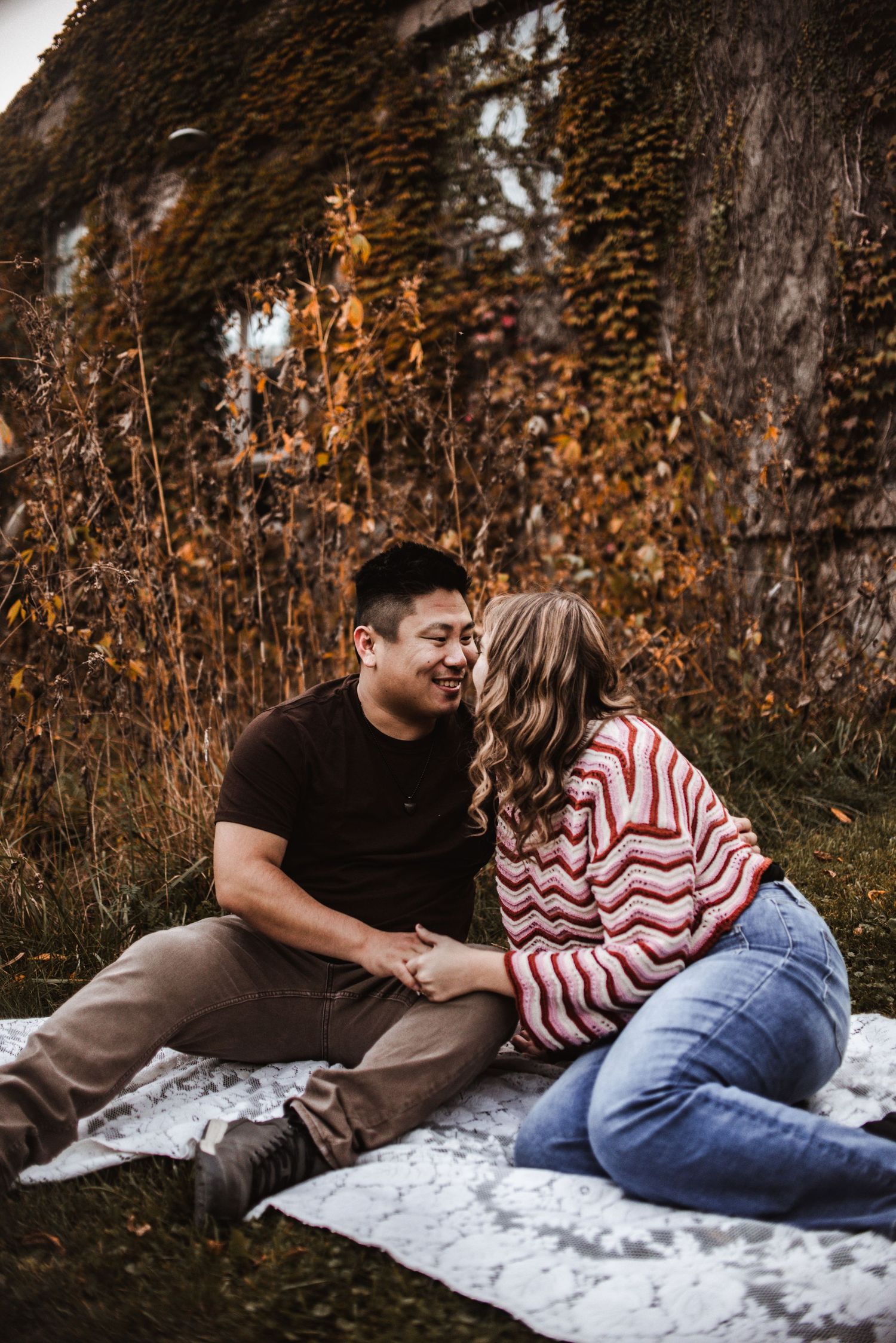 Couple sharing a tender moment while sitting on blanket outdoors surrounded by autumn foliage.