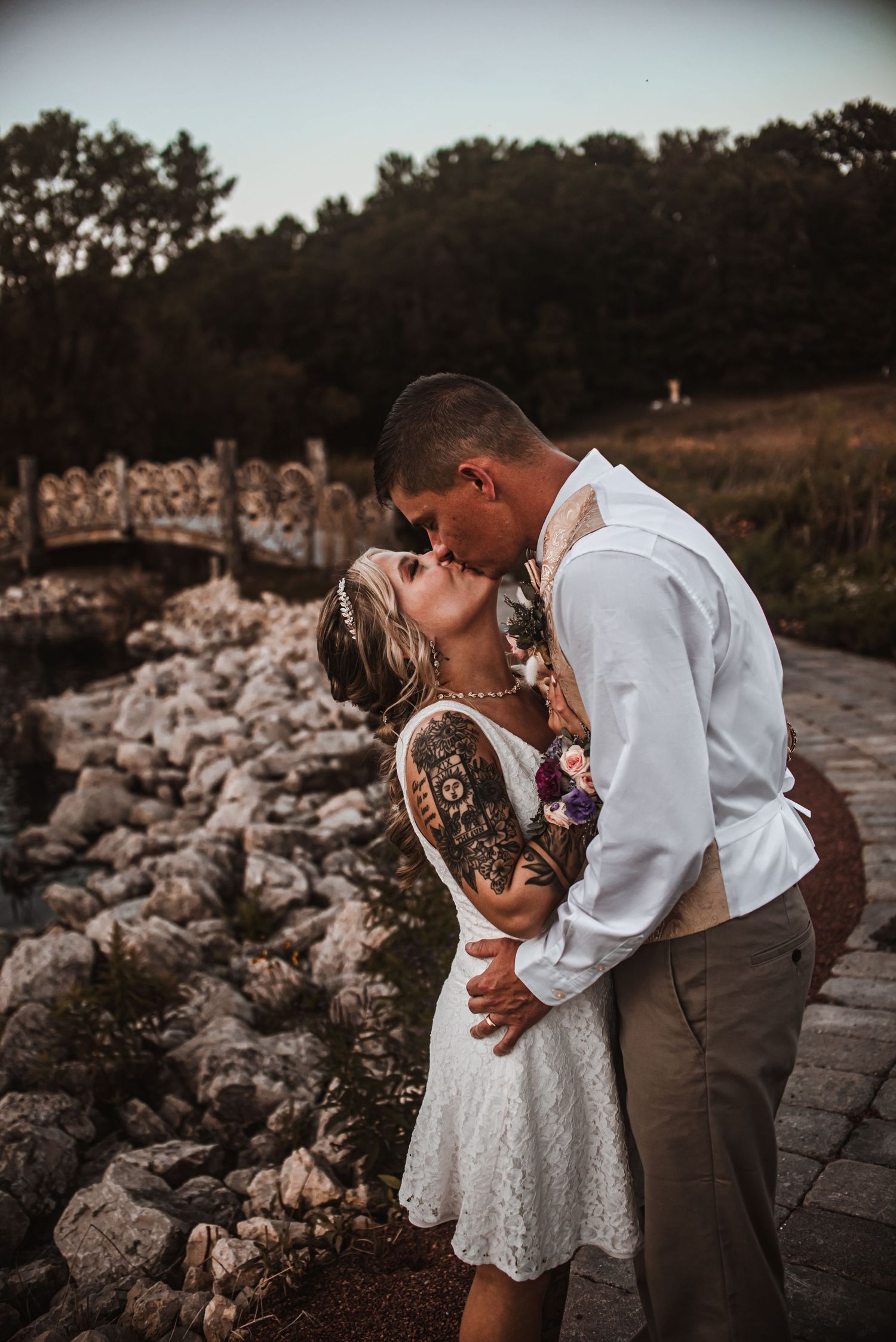 Romantic couple sharing intimate kiss on stone bridge during sunset.