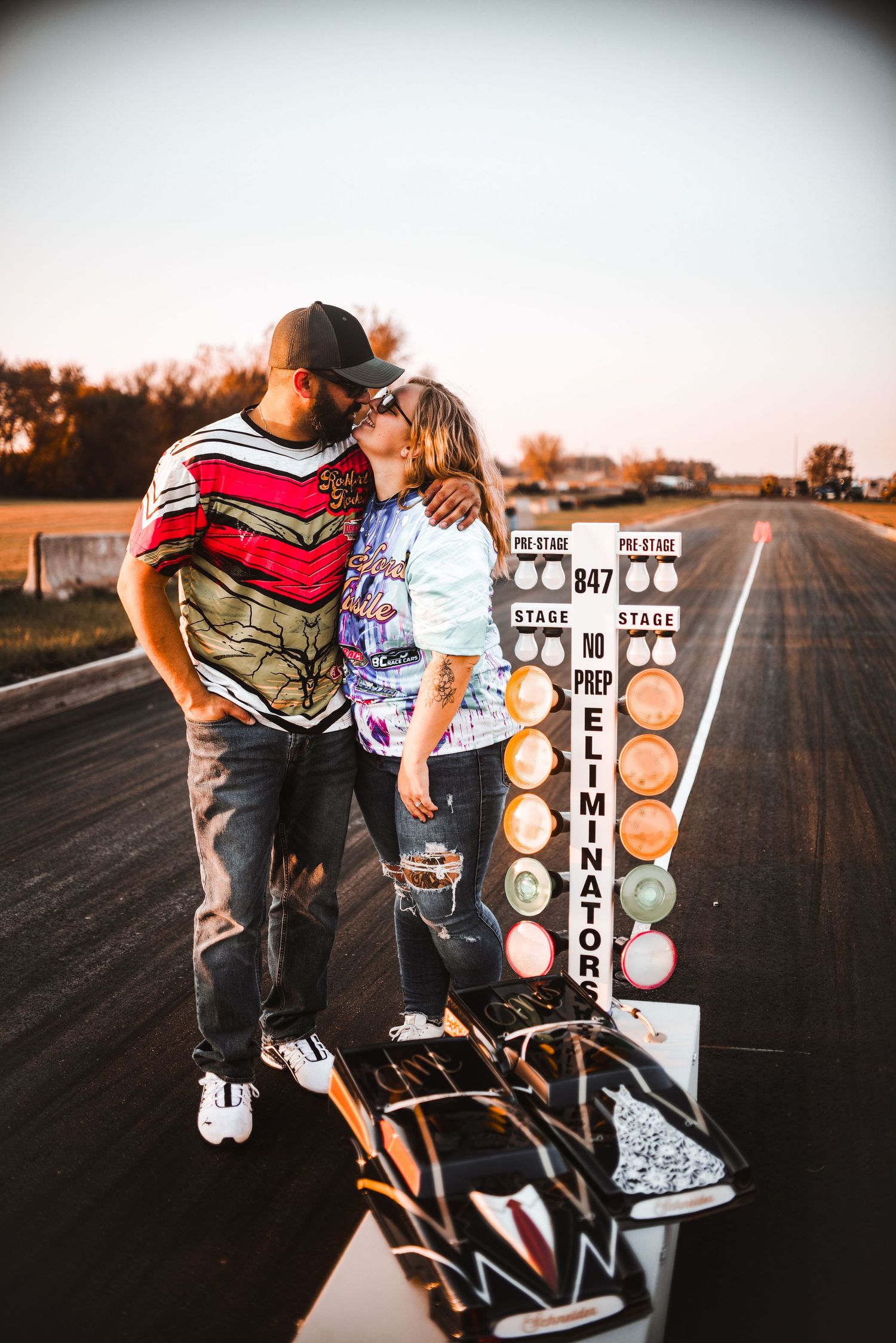Couple embracing near drag racing Christmas tree starting light system at dusk.