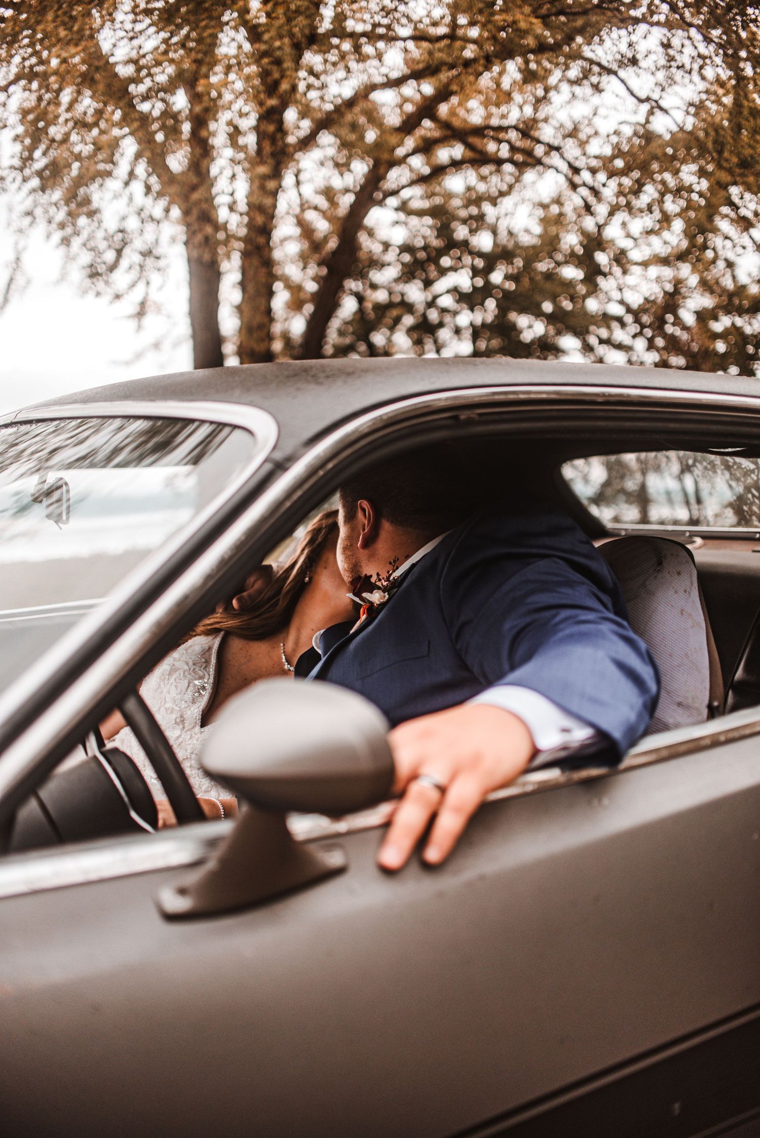 A romantic moment captured through a car window during a wedding day.
