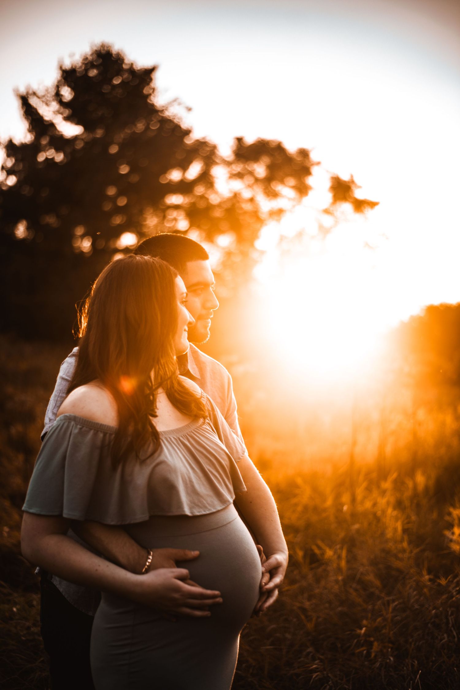 Silhouette of pregnant woman at sunset holding her belly in a tender maternity pose.