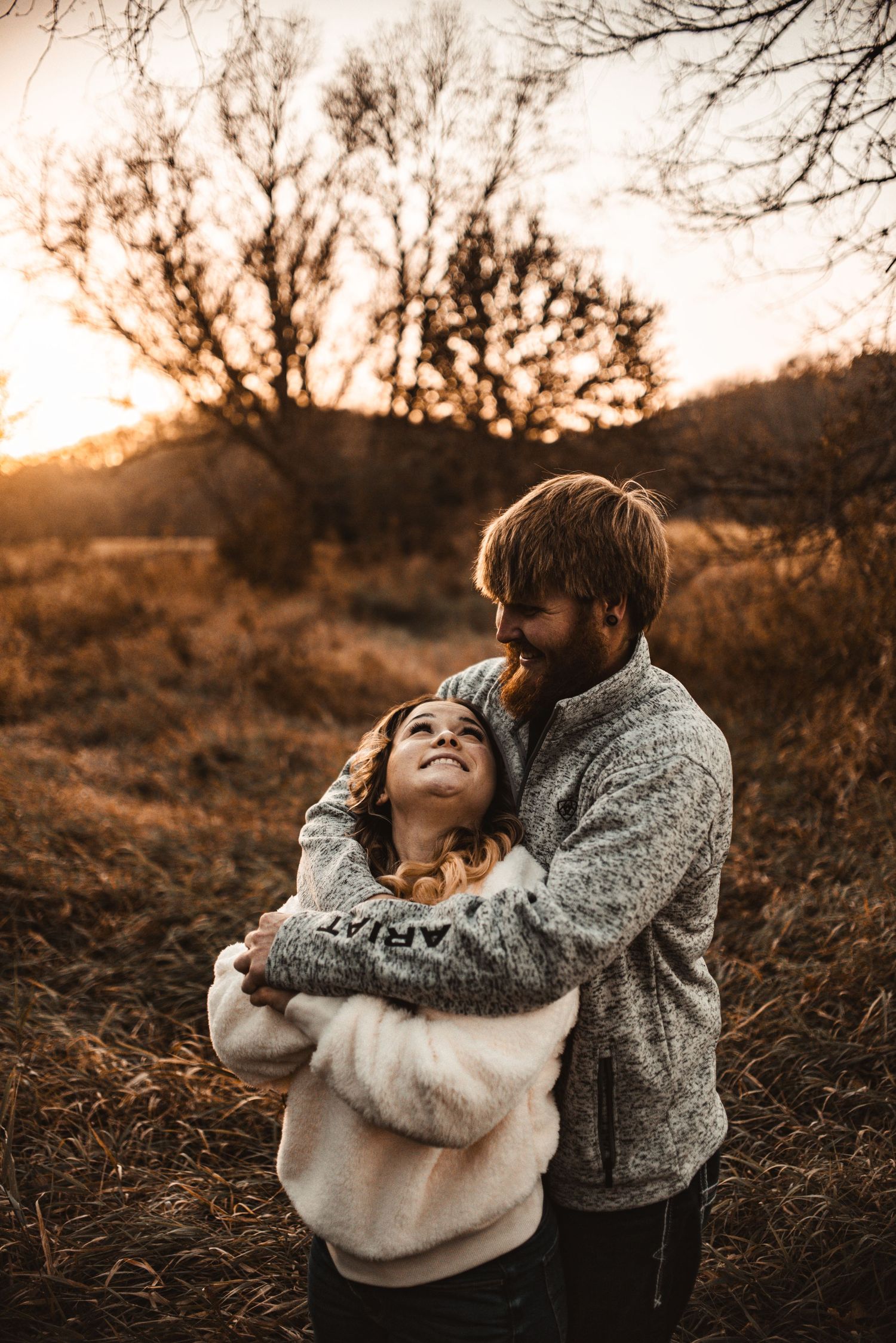 A romantic couple wearing cozy sweaters embrace outdoors during a warm golden sunset in autumn.