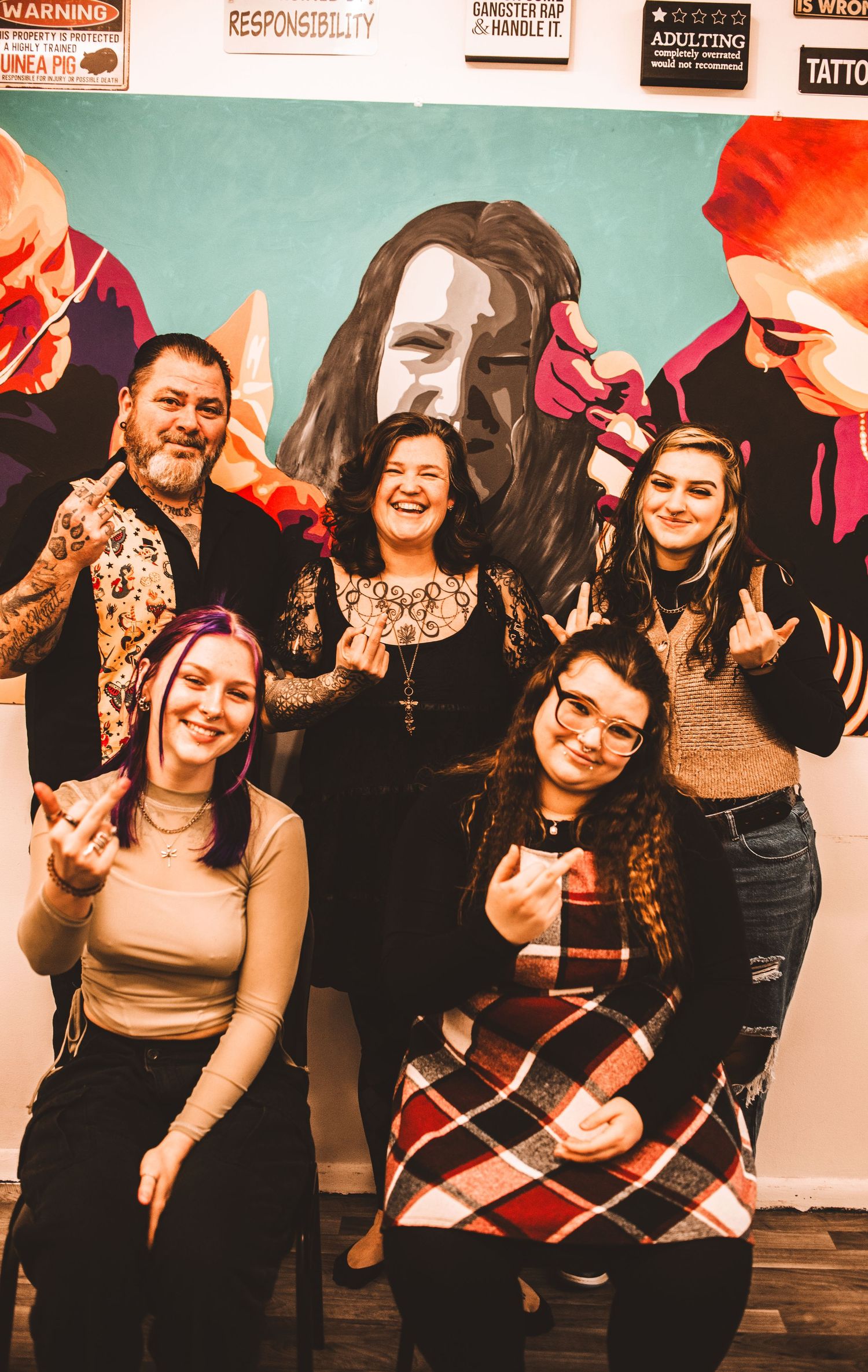 Group posing together in front of a vibrant wall mural with rock and roll hand gestures.