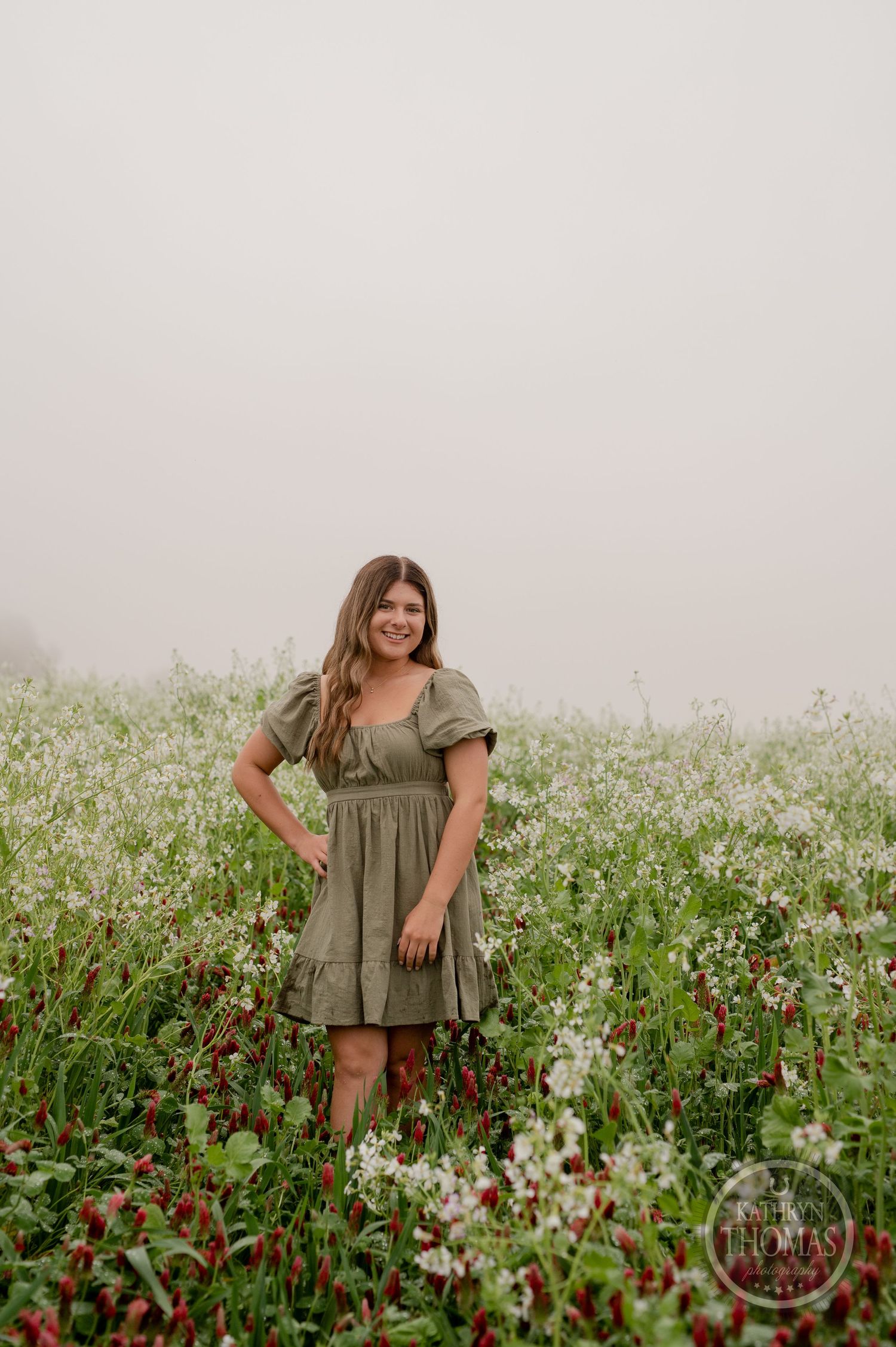 A dreamy meadow scene with someone wearing a sage green dress among red and white wildflowers.