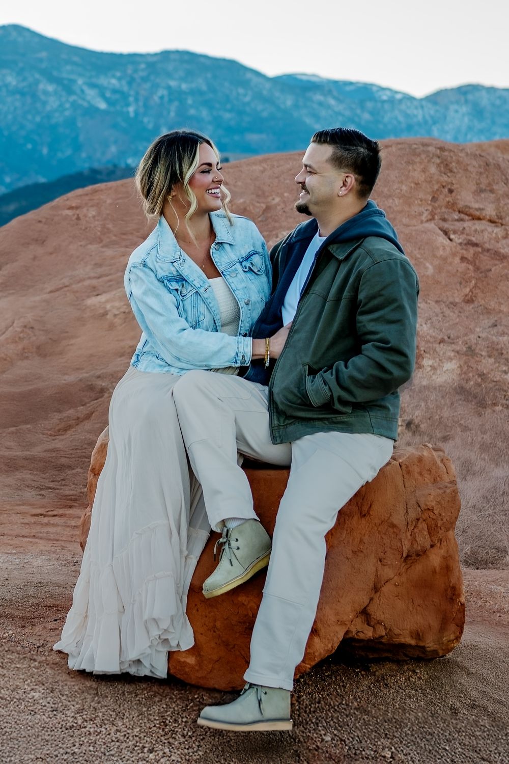 Casual engagement photo on red rocks with mountains and natural scenery in Colorado.