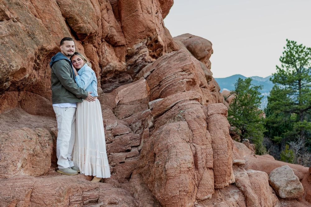 Couple stands against towering red rock formation with mountain vista in Colorado.