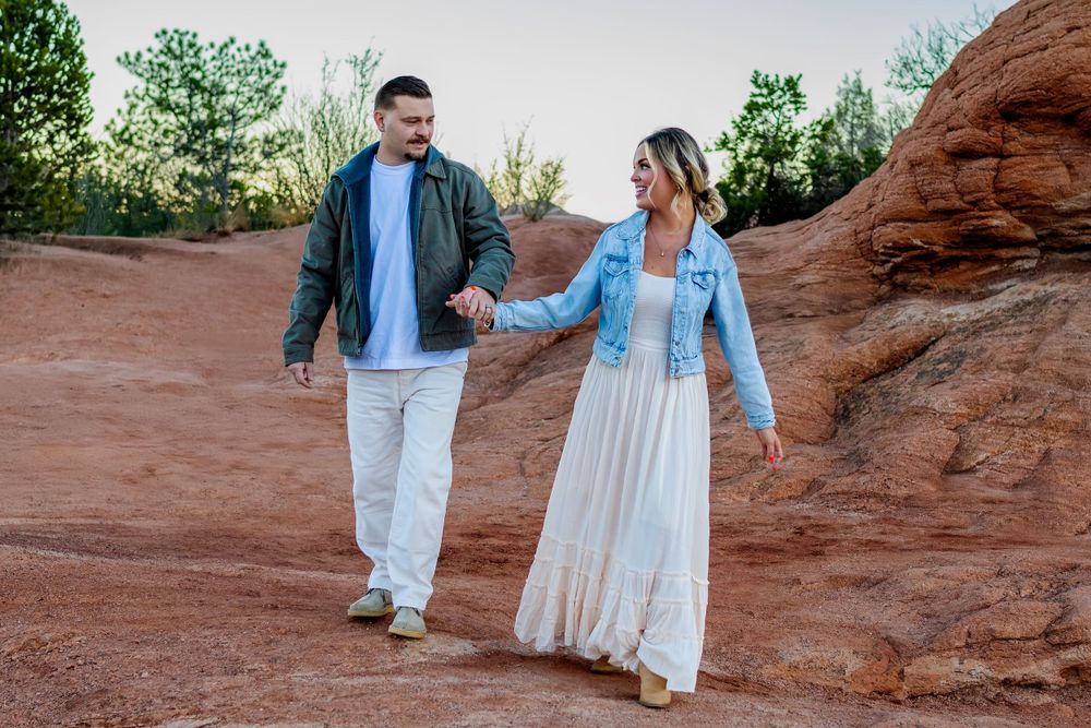A couple walks hand in hand on red rock formations wearing coordinating blue and white outfits.