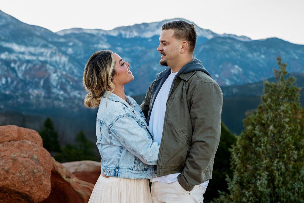 A couple shares a joyful moment together with mountain peaks and evergreens in the background.