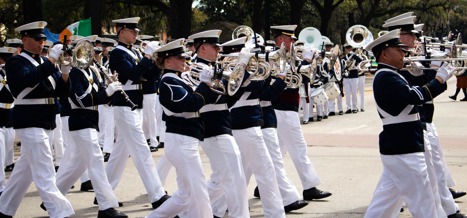 Marching band members in white uniforms performing during a parade.