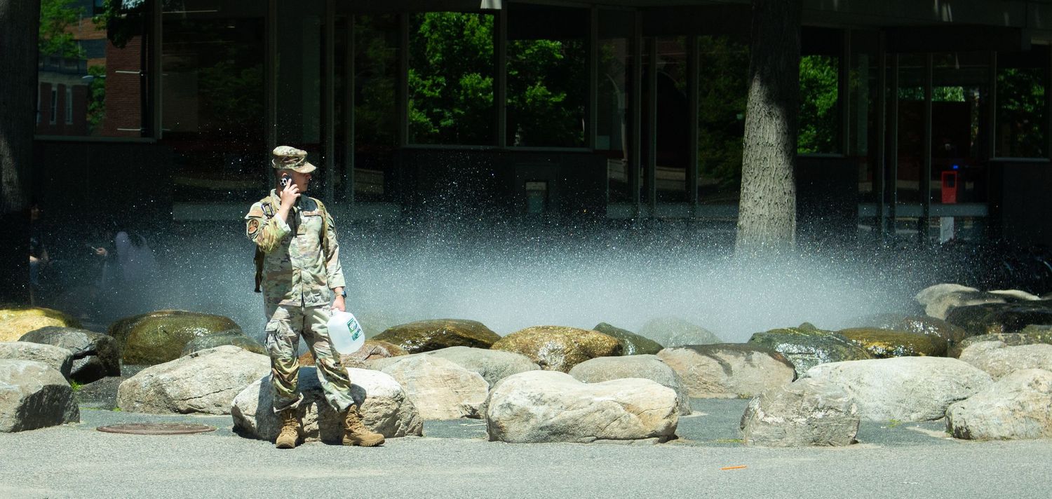 Soldier walking among large rocks near a misty fountain in an urban park setting.