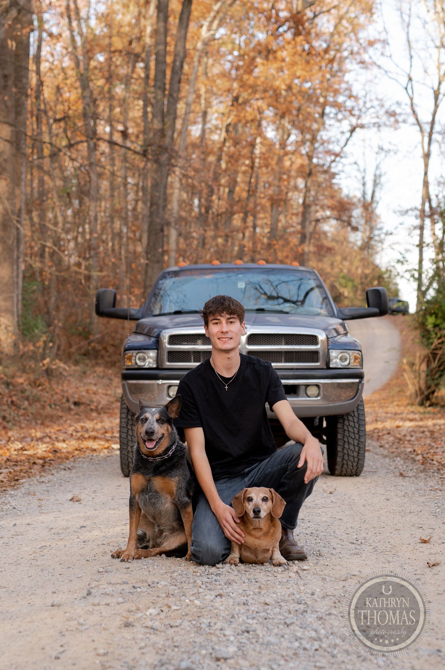 Person posing with German Shepherd and Beagle in front of Dodge Ram truck during autumn.