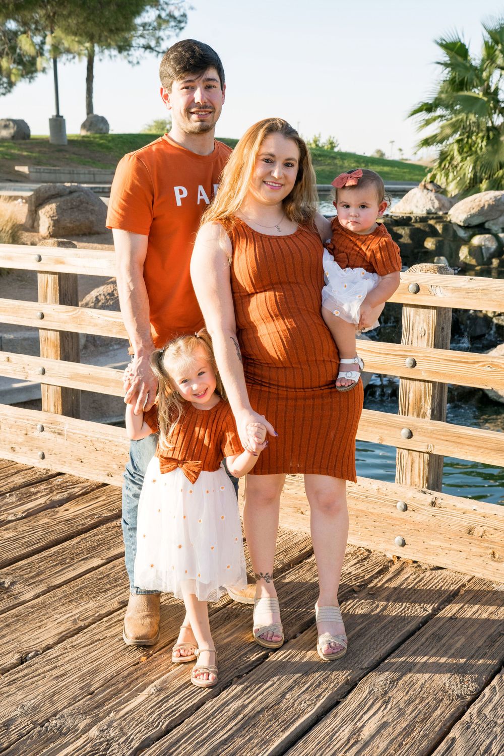 A family wearing coordinating orange outfits poses together on a wooden deck.