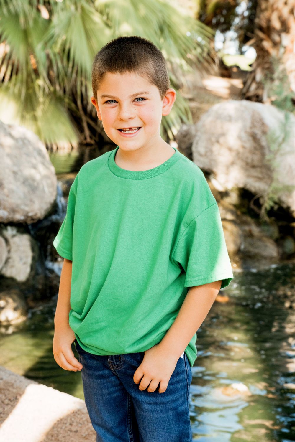 A young boy in a bright green t-shirt poses by a decorative rock water feature.