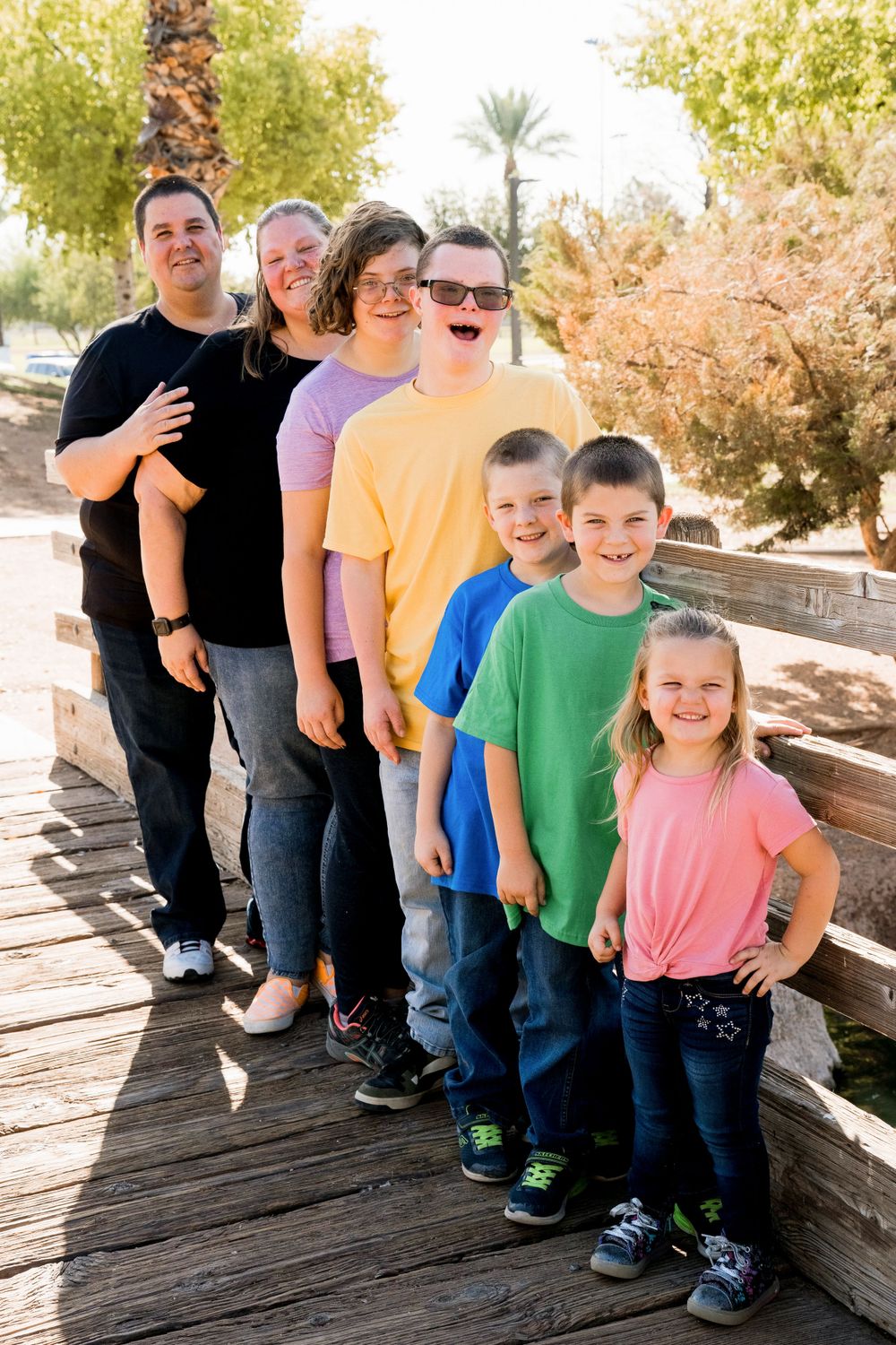 Line of family members pose from tallest to shortest on wooden boardwalk in colorful casual attire.