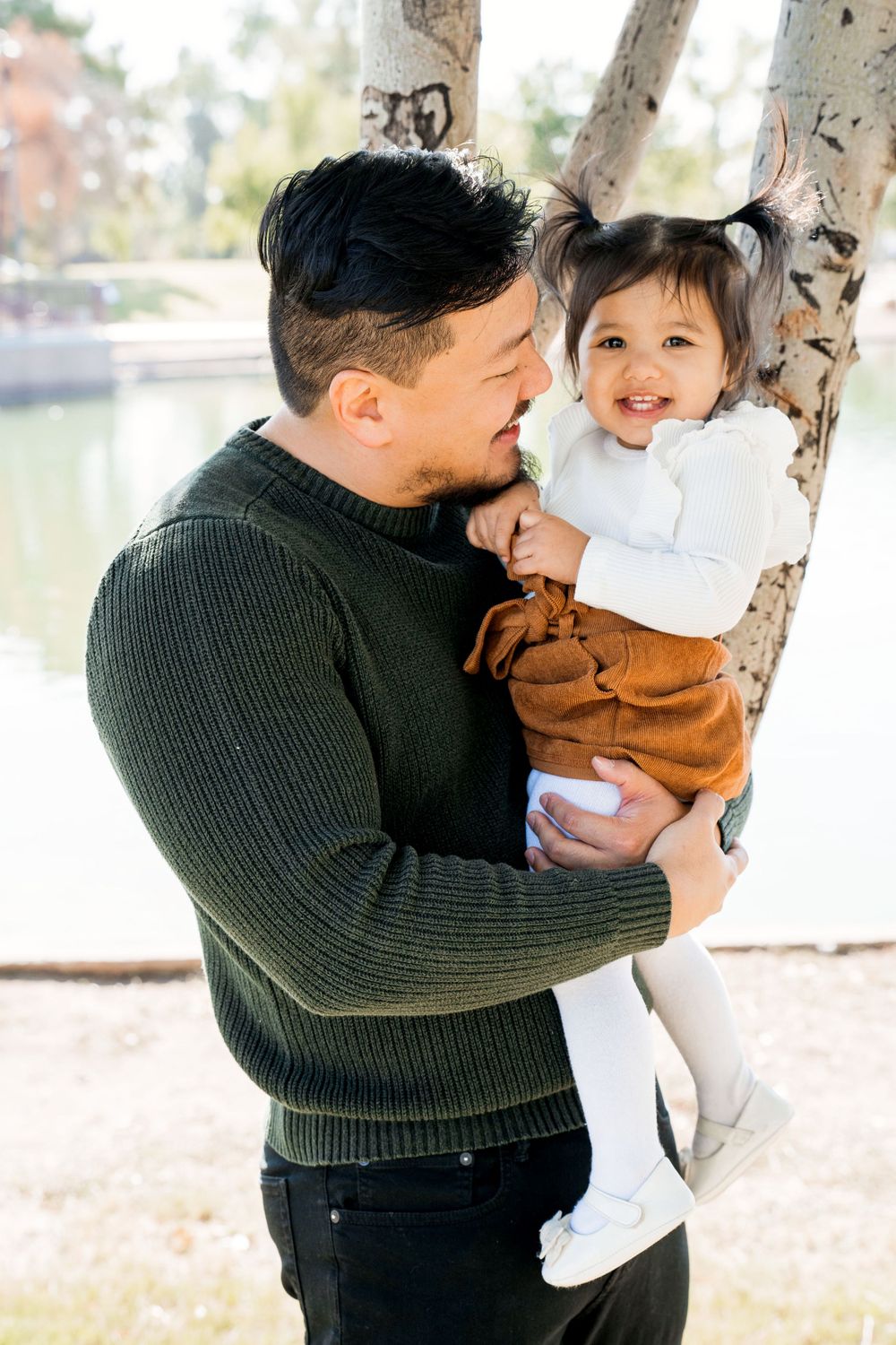 A parent and child share a tender moment next to a tree in the park.