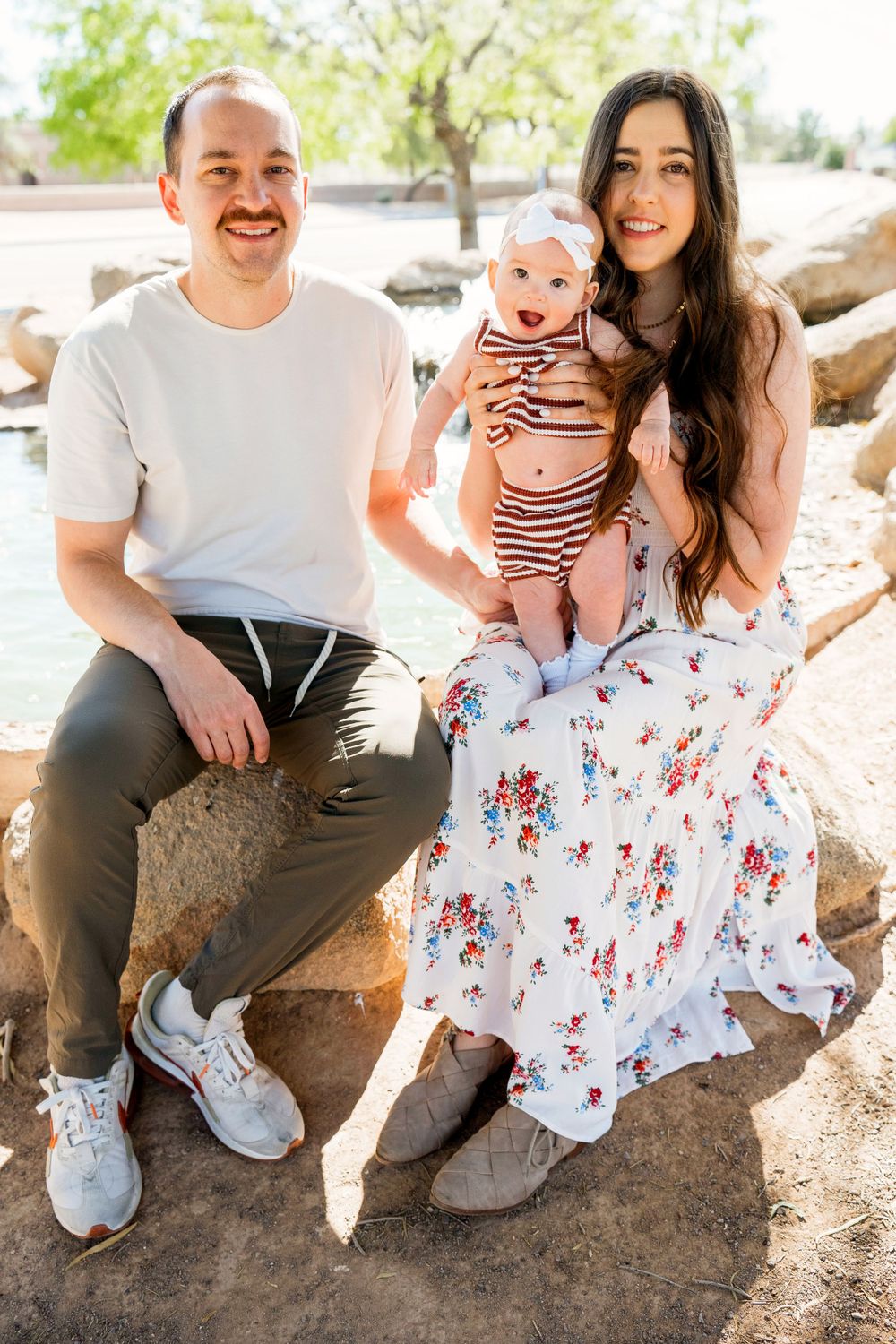 A family sitting on rocks outdoors in casual attire with a baby wearing a striped onesie.