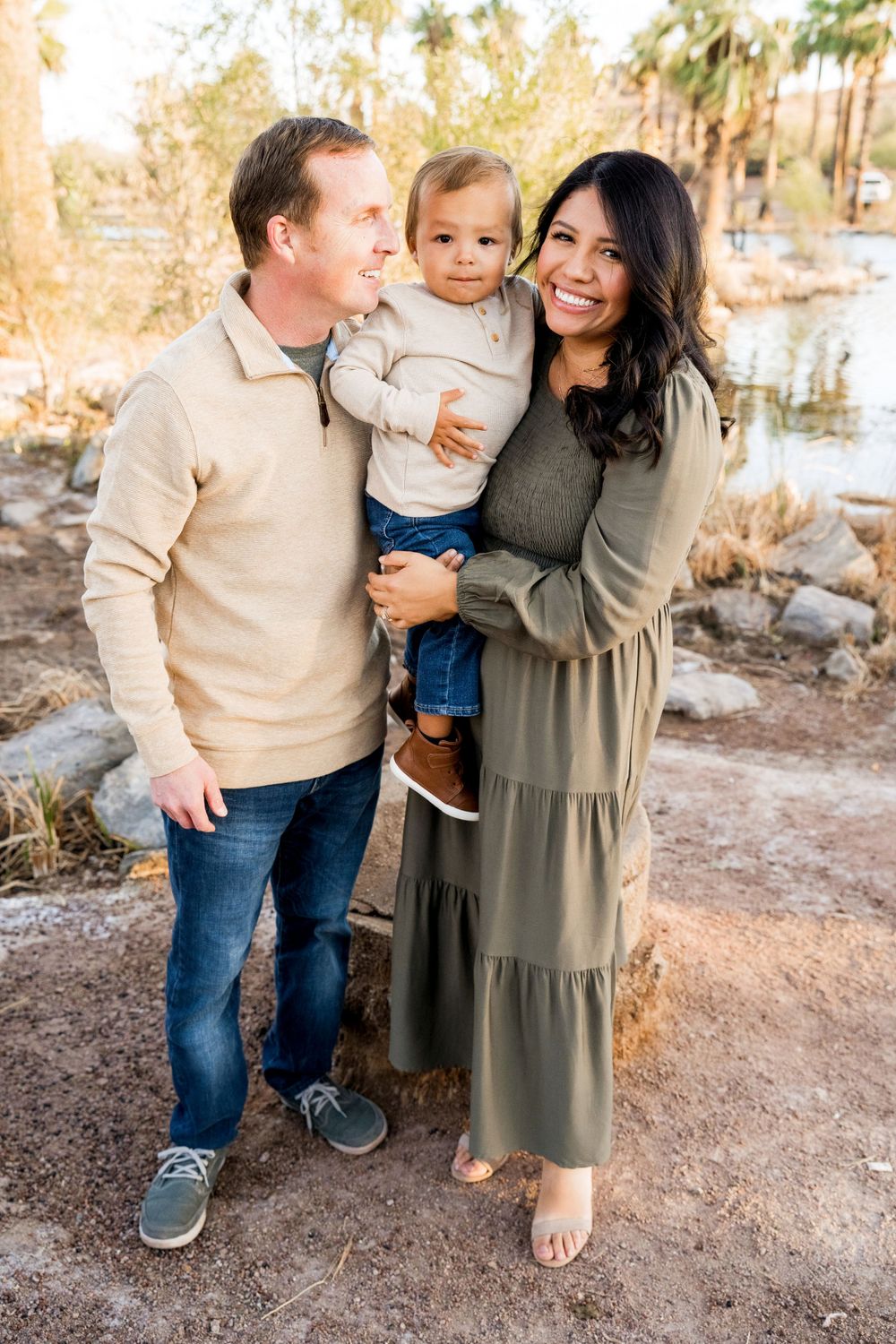 A family of three poses together outdoors in neutral-colored clothing.
