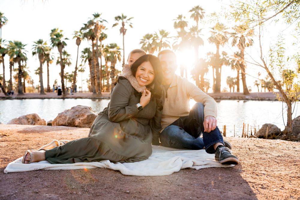 Two people sharing a romantic moment on a blanket at sunset with palm trees in the background.