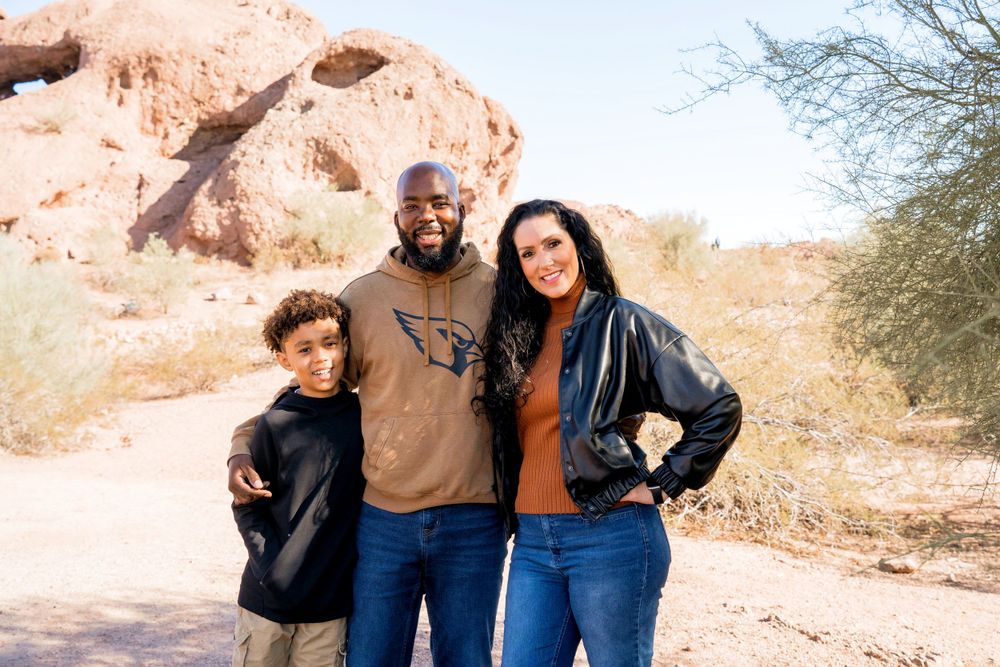 Family of three posing together in front of red rock formations in a desert landscape.