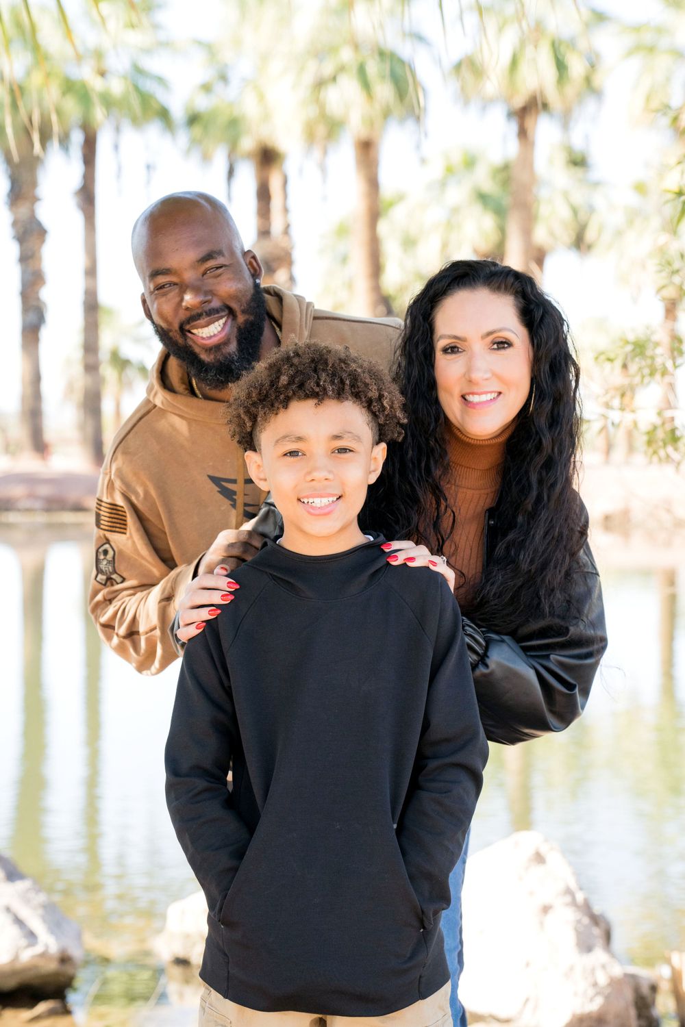 Family portrait in front of palm trees and a lake on a sunny day.