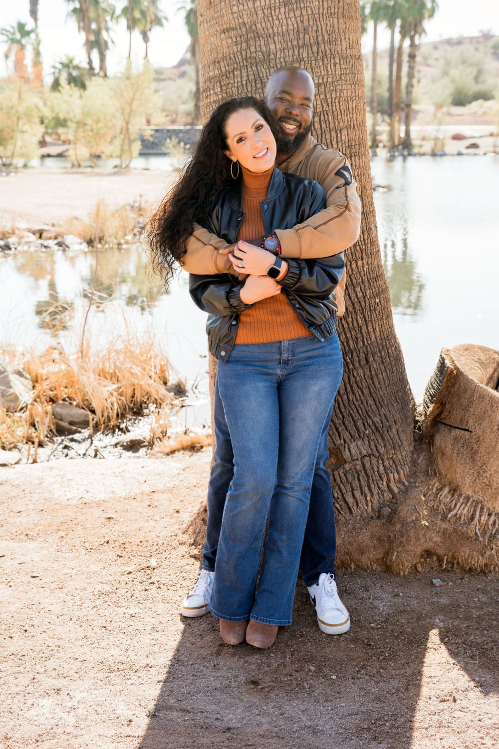 Couple embracing while standing against a palm tree trunk in a scenic outdoor setting.