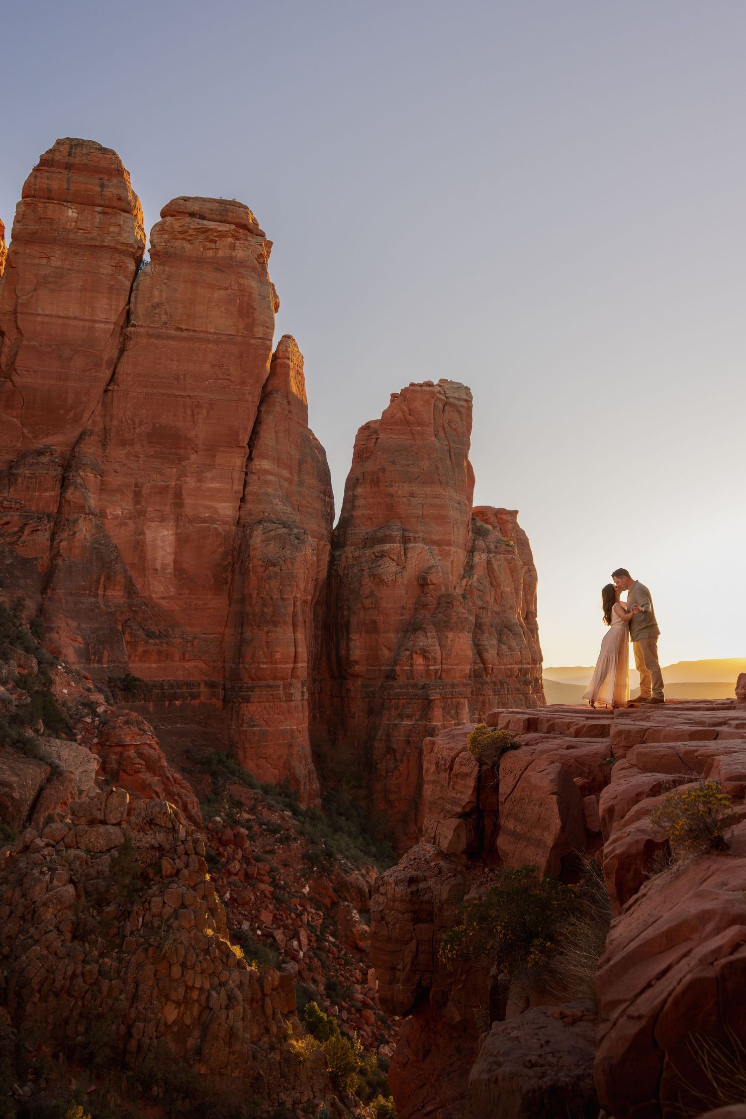 Couple sharing romantic kiss atop dramatic Sedona red rock spires at golden hour sunset.