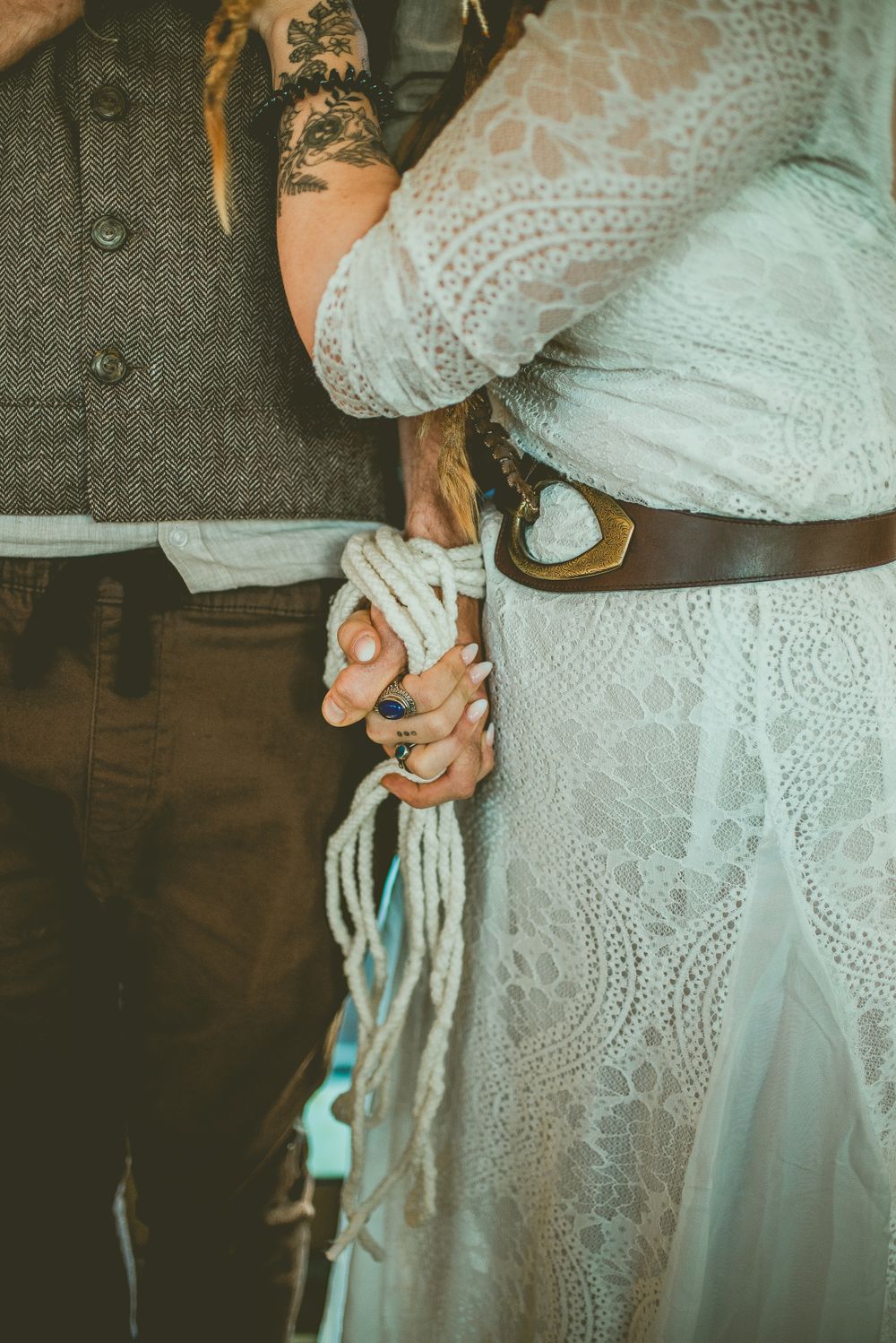 Close-up of hands performing traditional handfasting ceremony with rope during wedding, showing lace dress and formal attire.
