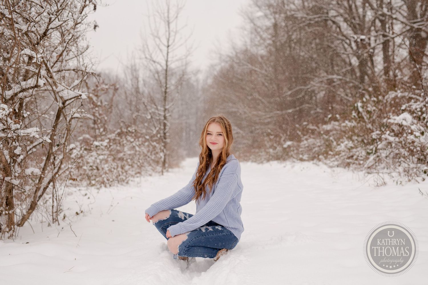 Candid winter photography with someone seated in the snow wearing casual denim and knitwear.