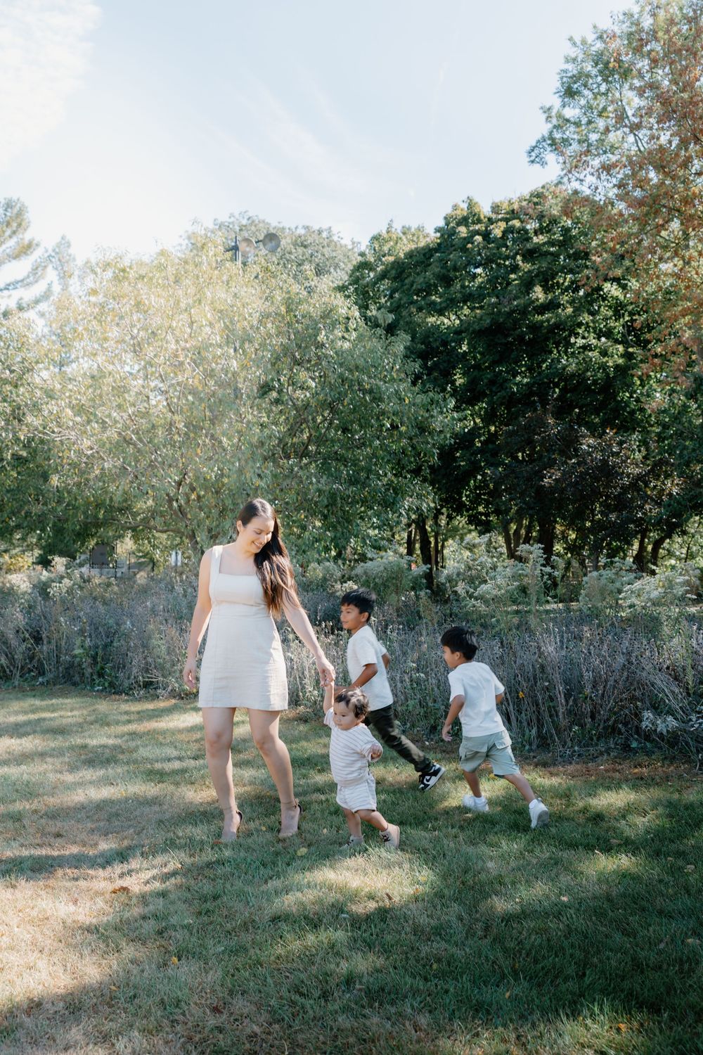 Family enjoying a playful moment together in a sunlit meadow with trees in the background.