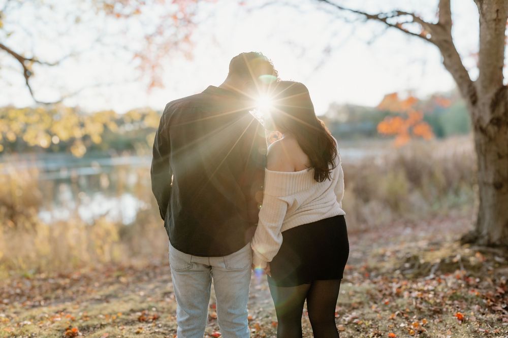 A couple embraces in a romantic autumn forest setting with golden sunlight filtering through the trees.
