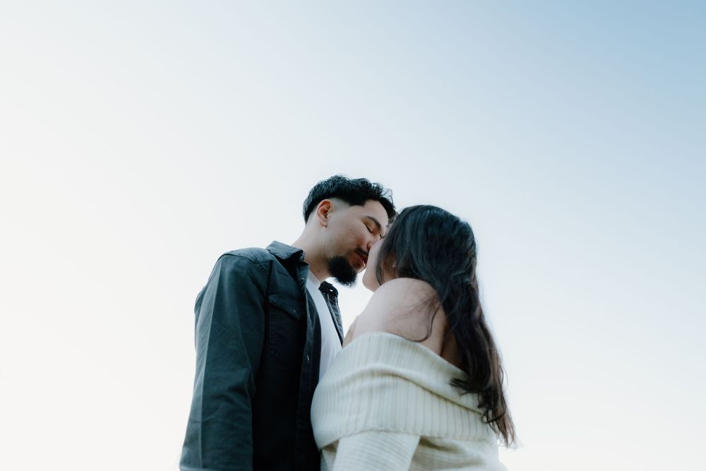 A romantic couple sharing a tender kiss against a bright blue sky background.