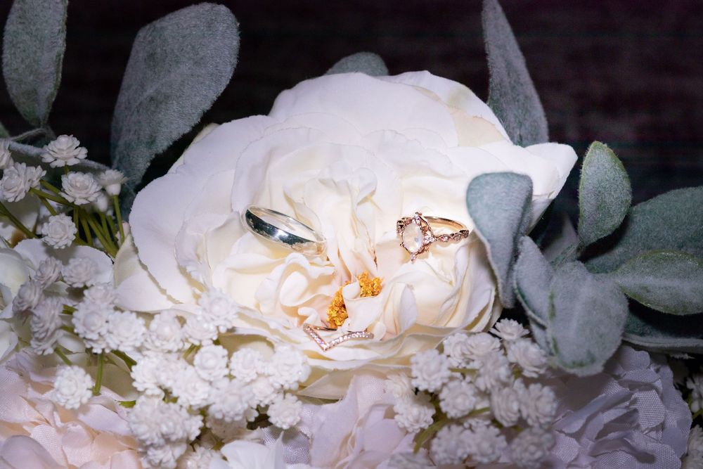 Two gold wedding rings rest elegantly on a white rose bouquet with eucalyptus leaves and baby's breath.
