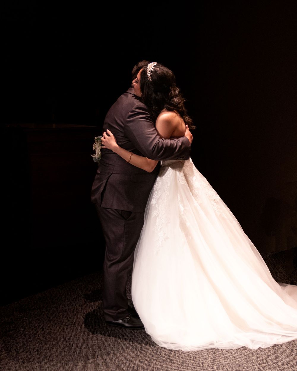 A bride and groom share a romantic embrace during their first dance, dressed in a white gown and dark suit.