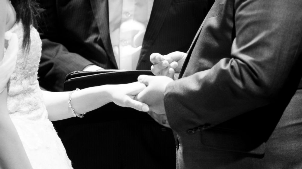 Black and white photo of a couple exchanging wedding rings during a ceremony.