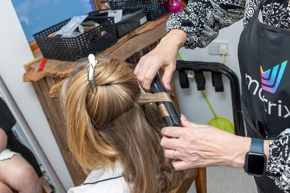 An image showing a person's hands styling a woman's blonde hair using a hair styling tool.