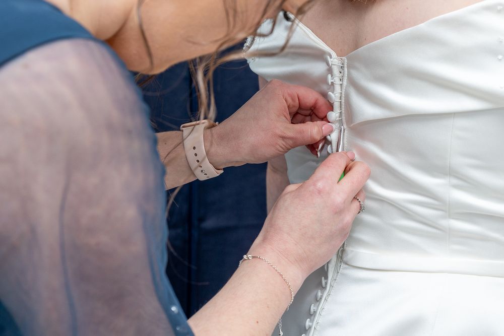 A person's hands are seen fastening the buttons on a wedding dress.