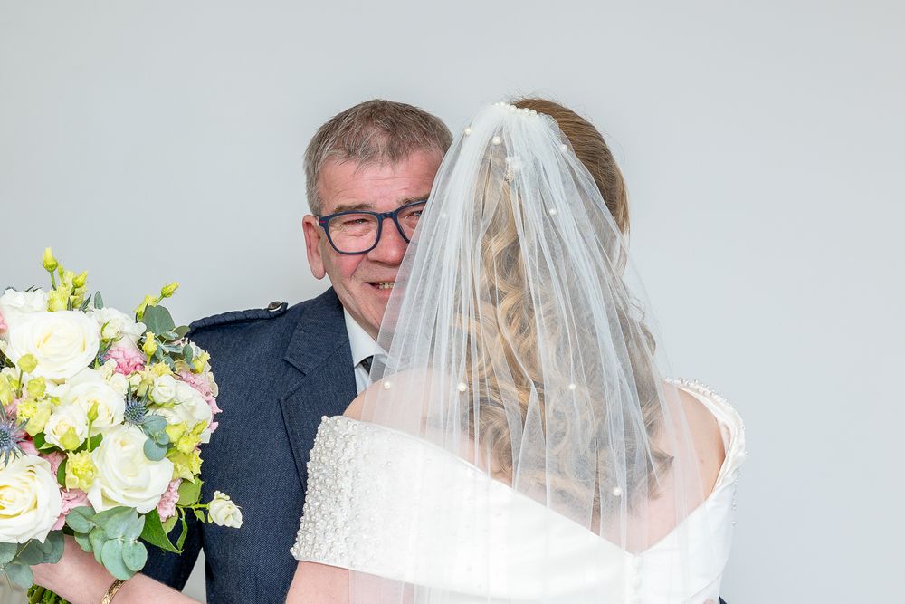 A bride and groom embrace each other on their wedding day, with the bride wearing a white wedding dress and veil.