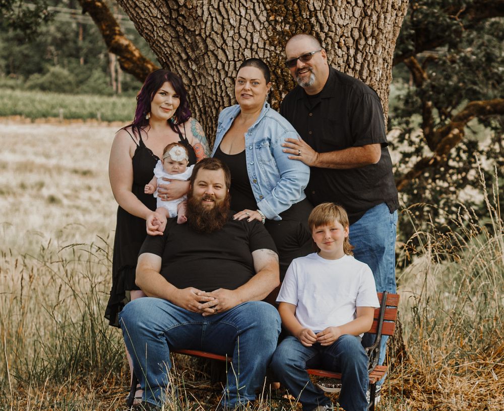 A multigenerational family poses together under a large oak tree in a sunny field.