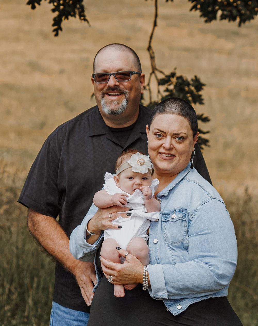 A smiling couple proudly holds their newborn baby girl outdoors in a golden field.